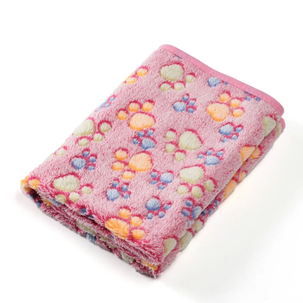 A pink fleece pet blanket featuring a paw print pattern with multicolored paw prints.