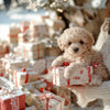 A fluffy light brown puppy is sitting on a wrapped gift box in a festive holiday setting.