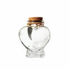 A clear glass heart-shaped jar with a cork stopper and a small metal charm for storing pet hair.