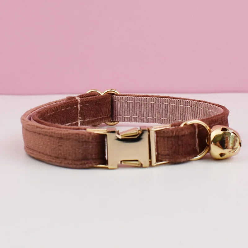 A brown velvet cat collar with a gold-toned buckle and bell on a white surface.