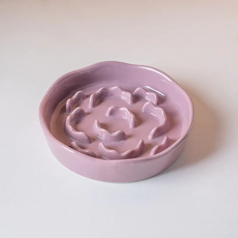 A pink ceramic pet bowl with a raised neck-safe design is shown on a white surface.