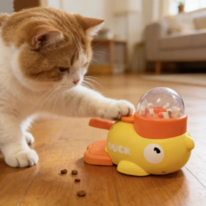 A ginger and white cat is interacting with a yellow duck slow feeder puzzle toy on a wooden floor.