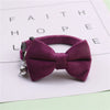 A deep purple plush velvet pet collar featuring a bow and a silver bell, resting on a white background.