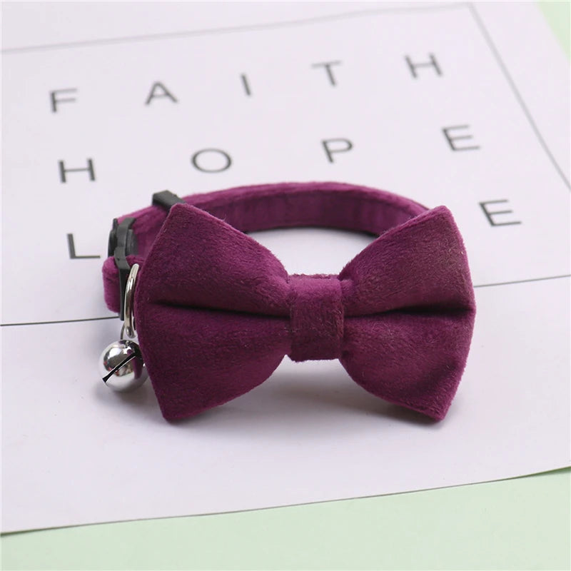 A deep purple plush velvet pet collar featuring a bow and a silver bell, resting on a white background.