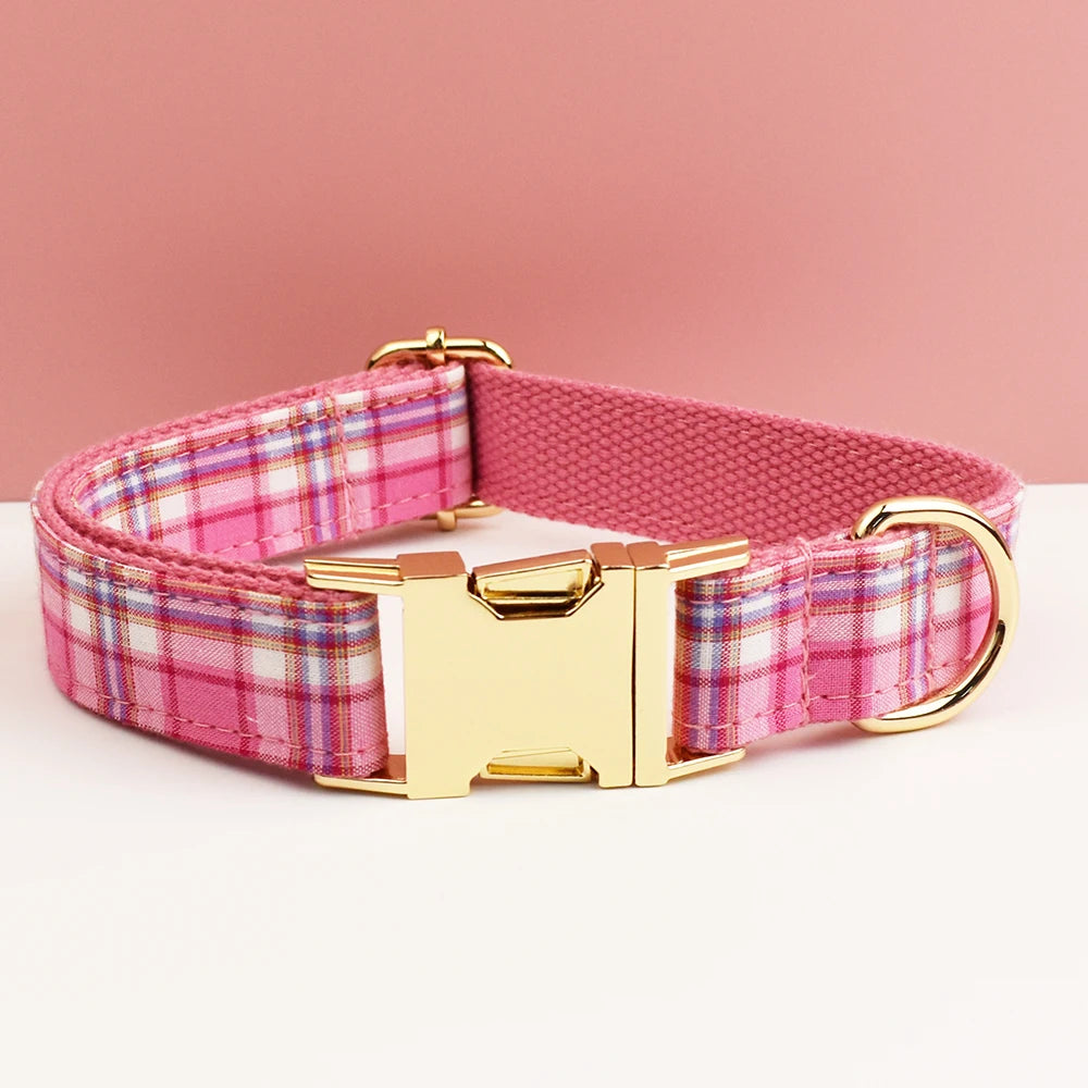 A pink plaid dog collar with a gold buckle is displayed on a white surface.