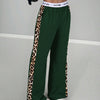 A woman wearing dark green leopard print high-waist wide leg pants and a white top.