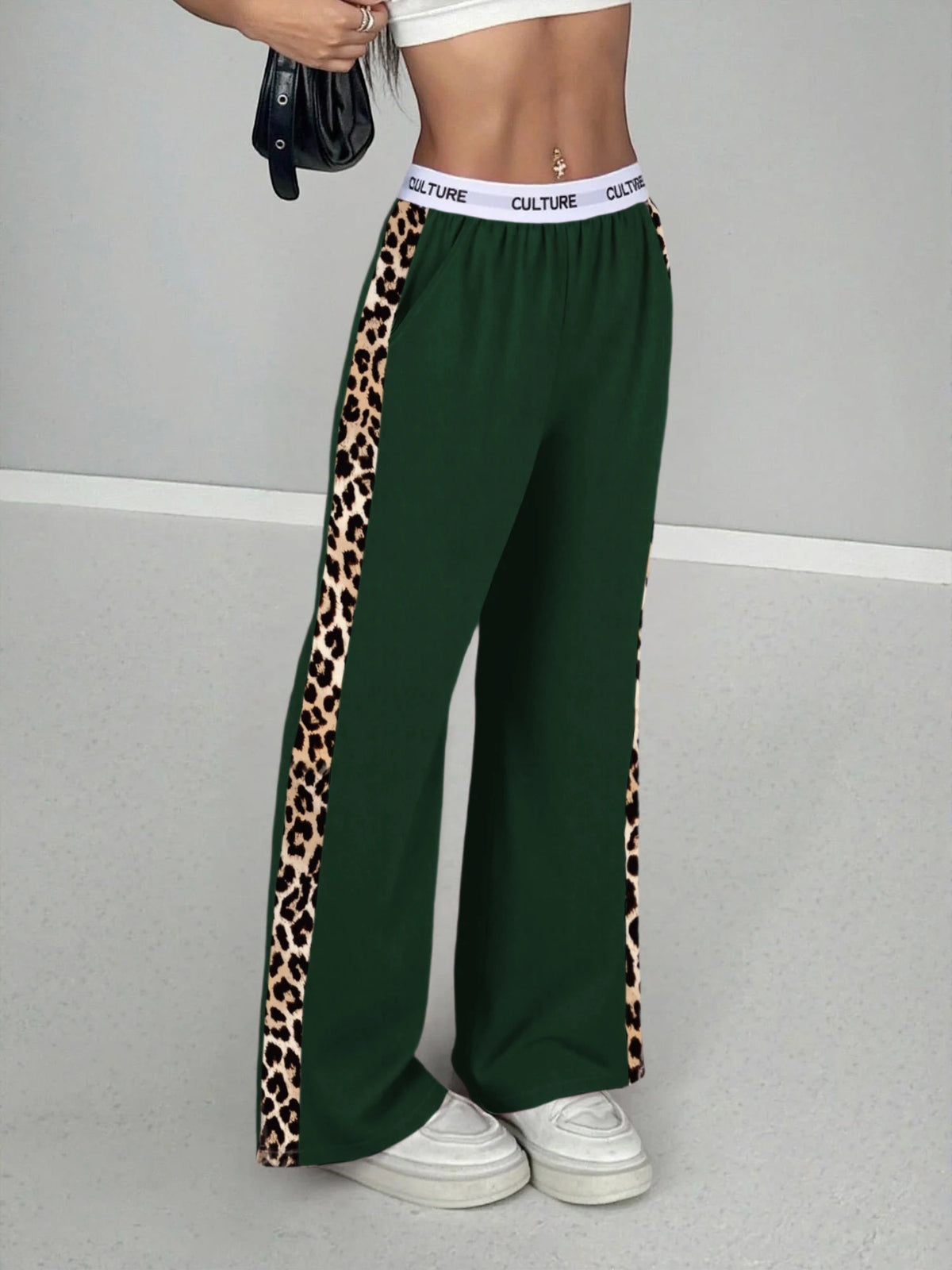A woman wearing dark green leopard print high-waist wide leg pants and a white top.