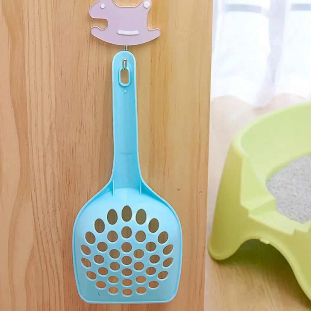 A light blue plastic cat litter scoop hanging on a wooden surface, with a pink piece attached above it.