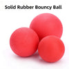A close-up view of a bright red solid rubber bouncy ball resting on a white surface.