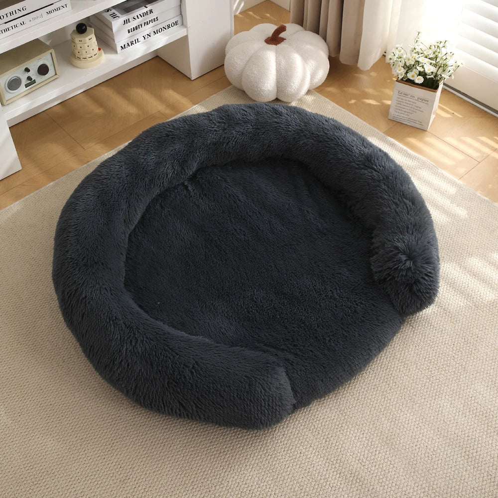 A round, dark gray ultra-soft dog bed with a fluffy exterior resting on a light beige rug.