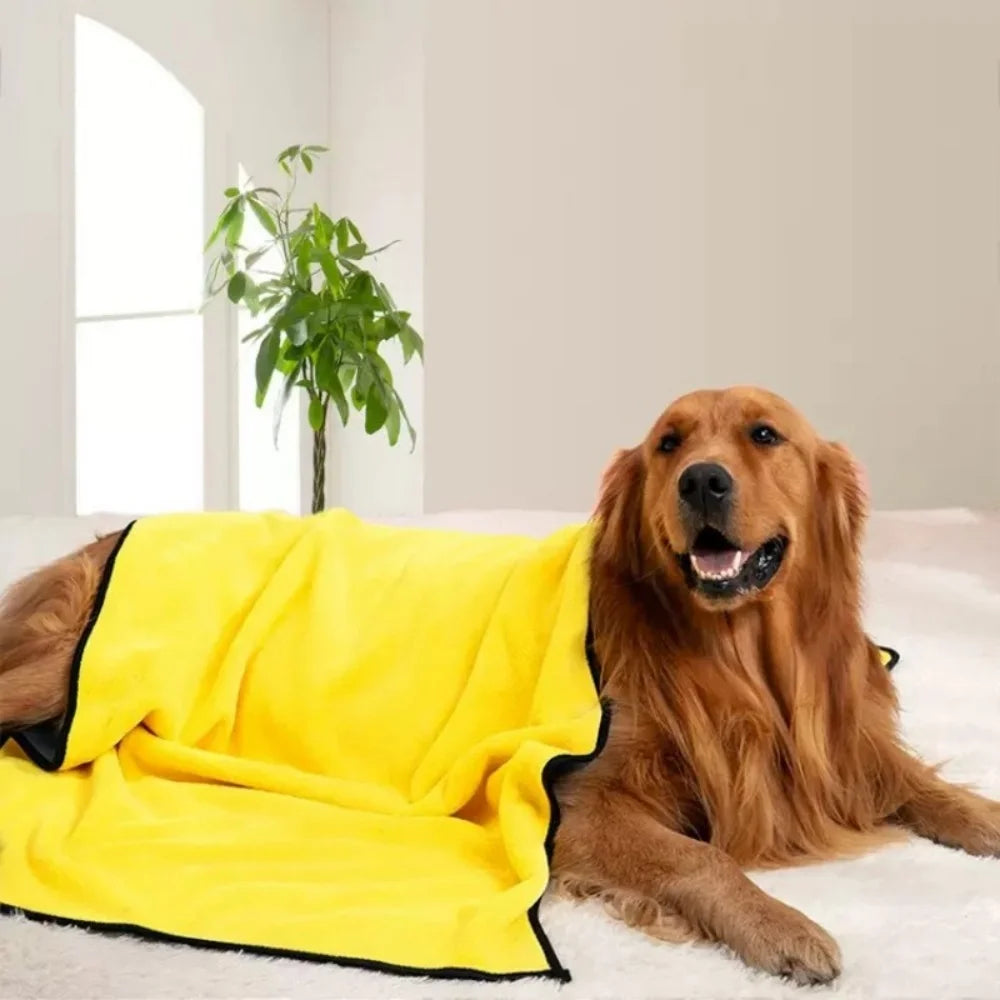 A golden retriever lies on a white surface next to a bright yellow ultra-absorbent pet drying towel.