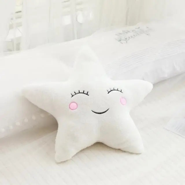 A white star-shaped plush pillow with embroidered eyes and smile resting on a white bed.