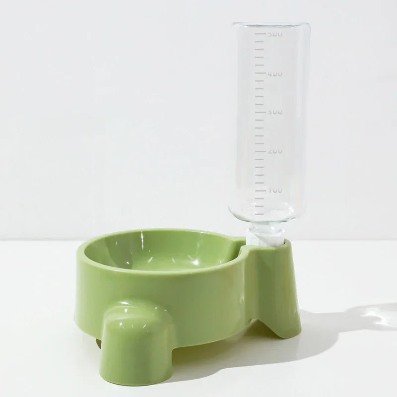 A light green automatic pet water dispenser with a clear measuring tube sits on a white surface.