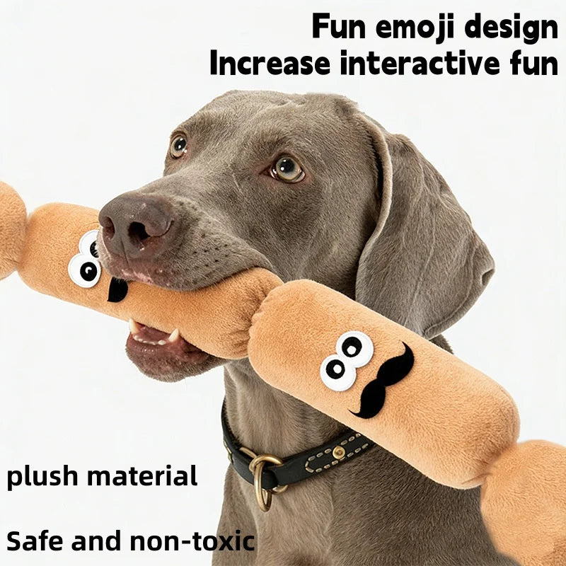 A gray dog holds a sausage-shaped plush toy with a black mustache and eyes.