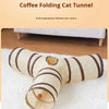 A beige folding cat tunnel with brown stripes is shown lying on a white fluffy towel.