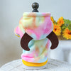 A pink and yellow plush fleece pet overalls for dogs and cats with a dark wooden top.