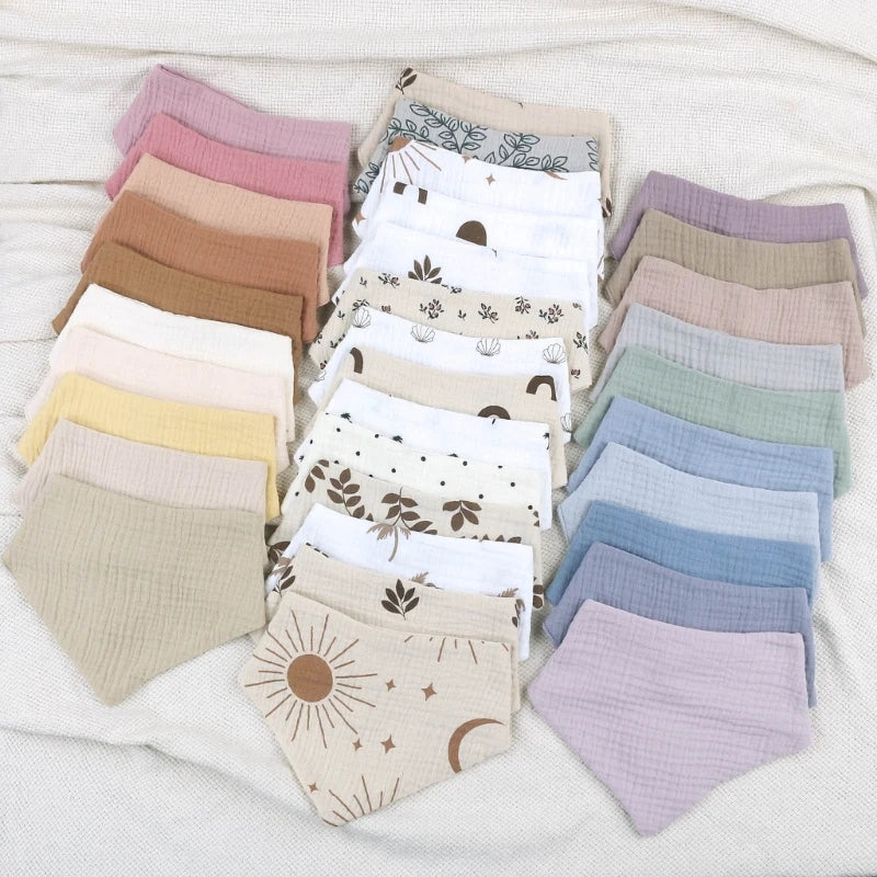 A collection of nine cotton baby bibs in various pastel colors and printed designs laid out on a white surface.