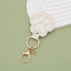 A light beige leather paw print airtag keepsake attached to a gold ring on a pale green surface.