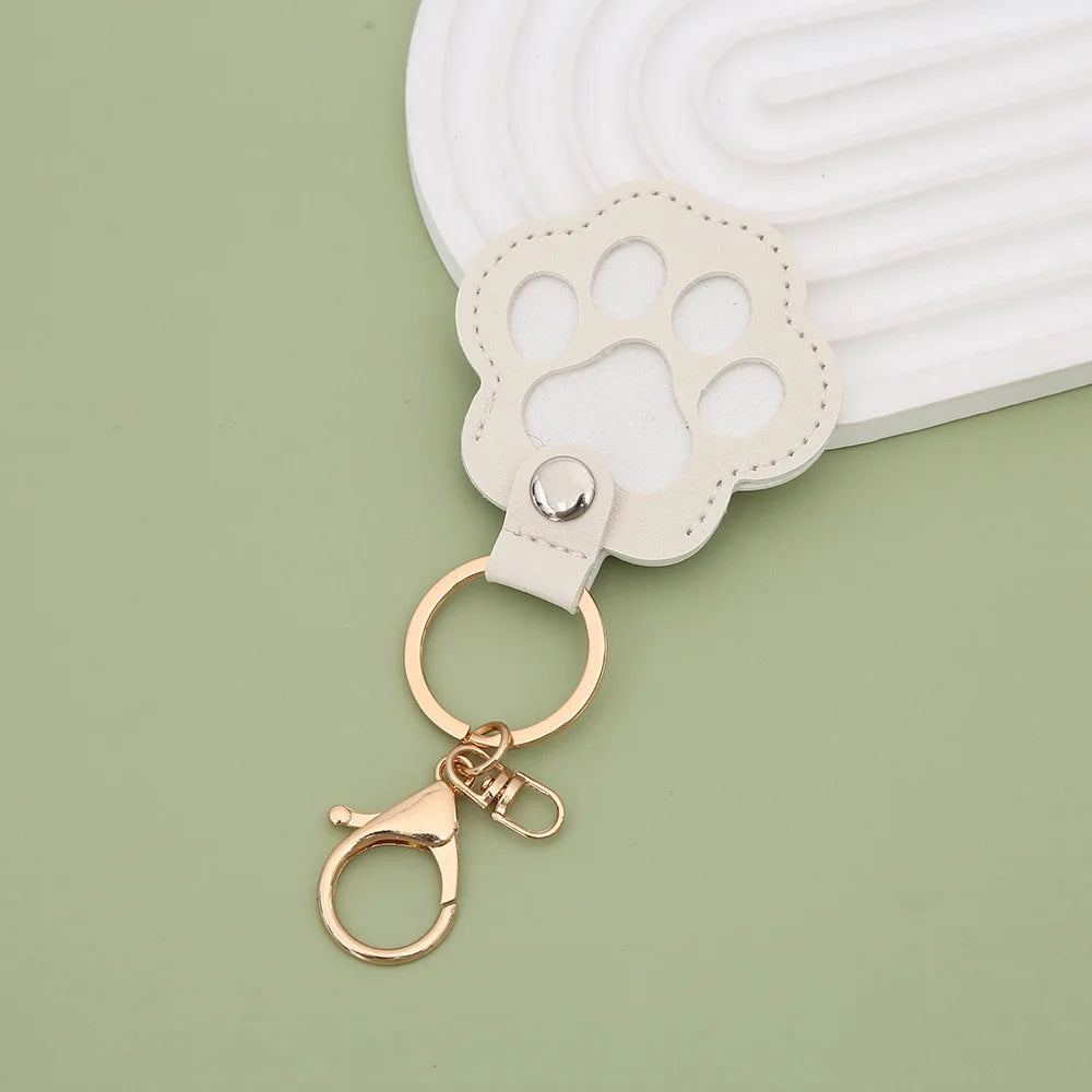 A light beige leather paw print airtag keepsake attached to a gold ring on a pale green surface.