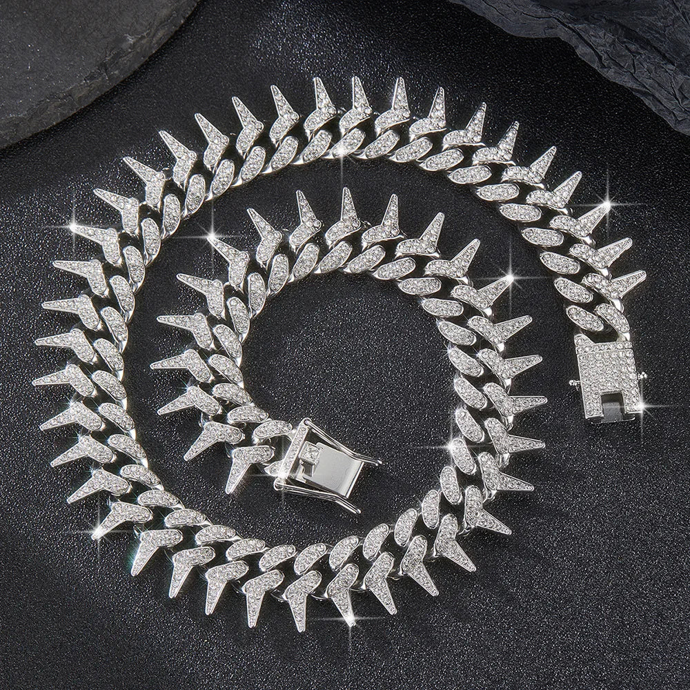 A silver spiked Cuban chain bracelet with diamond accents coiled on a dark surface.