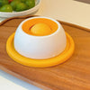 An interactive licking mat for pets featuring a white base and an orange feeding dome placed on a wooden board.