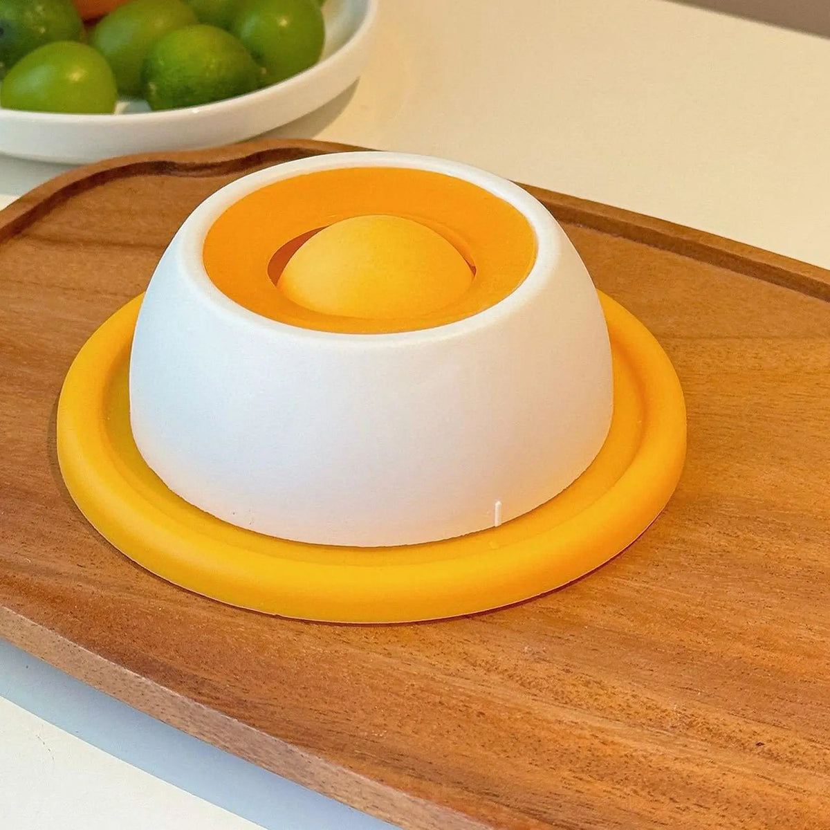 An interactive licking mat for pets featuring a white base and an orange feeding dome placed on a wooden board.