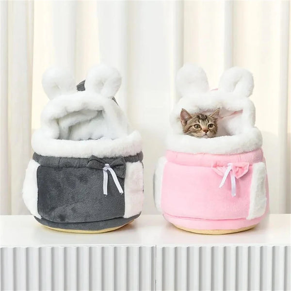 A pink winter warm pet carrier backpack with white fluffy ears and a small tabby cat inside.