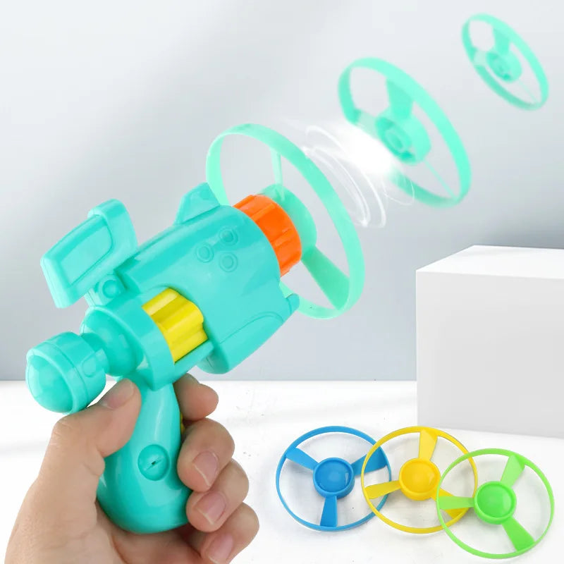 A hand holds a teal toy launcher with four replacement green and yellow flying discs spinning in the air.