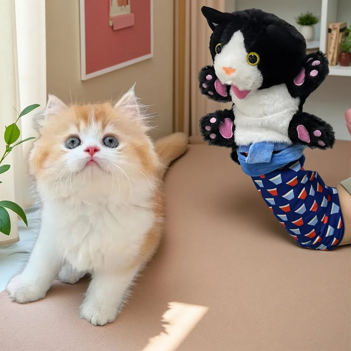 A fluffy orange and white kitten sits on a brown surface next to a black and white cat wrestling toy.