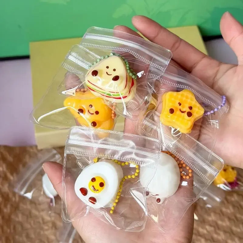 A hand holds several clear plastic bags containing squishy bread fidget toys shaped like eggs and toast.