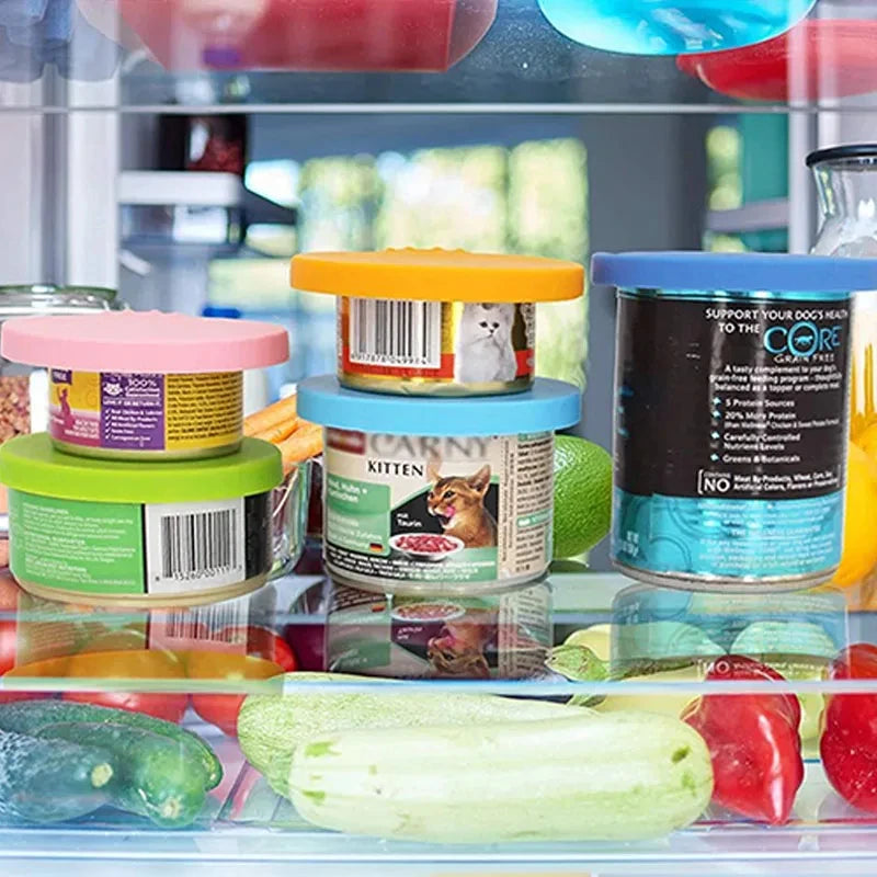 A collection of reusable silicone pet food can lids and spoons in various colors displayed in a glass container.