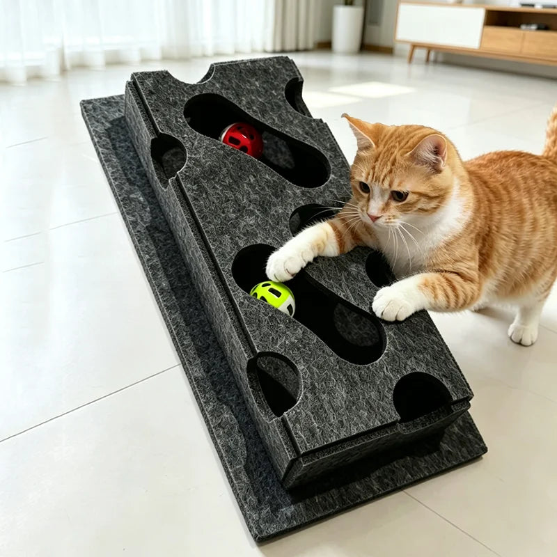 A tabby cat is interacting with an interactive puzzle toy box featuring a maze tunnel and a red ball.