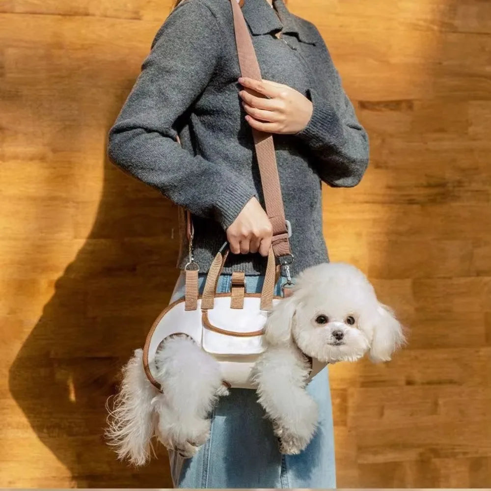 A person is holding a beige portable pet carrier sling bag with a brown strap and a small white fluffy dog.