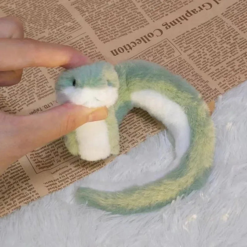 A hand holds a soft, bendable plush toy resembling a green snake with white markings against a background of old paper.