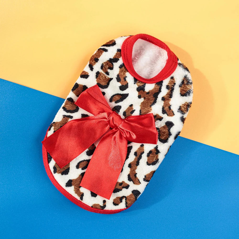 A warm knit pet sweater with a leopard print exterior and a red ribbon bow, set against a blue background.