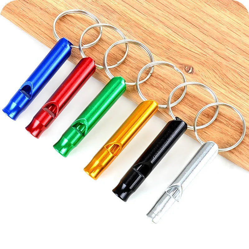A collection of colorful metal whistles with rings laid out on a wooden surface.