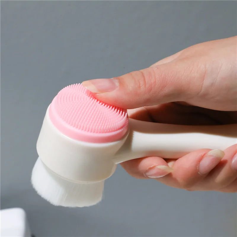 A hand holds a white silicone pet paw cleaner brush with a pink dual-sided silicone pad against a gray background.