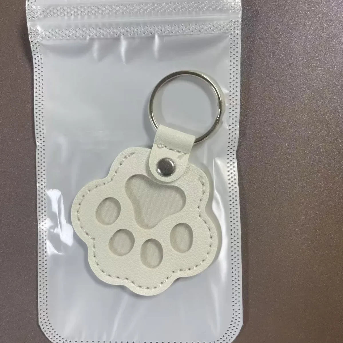 A light beige leather pet paw print keychain charm is visible inside a clear plastic pouch.