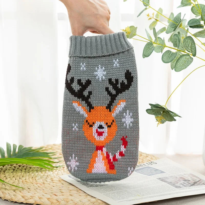 A knitted grey dog sweater with orange and white festive deer antlers is held by a hand.