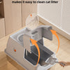 A stainless steel cat litter box with a flip cover design is shown being cleaned with a brush.