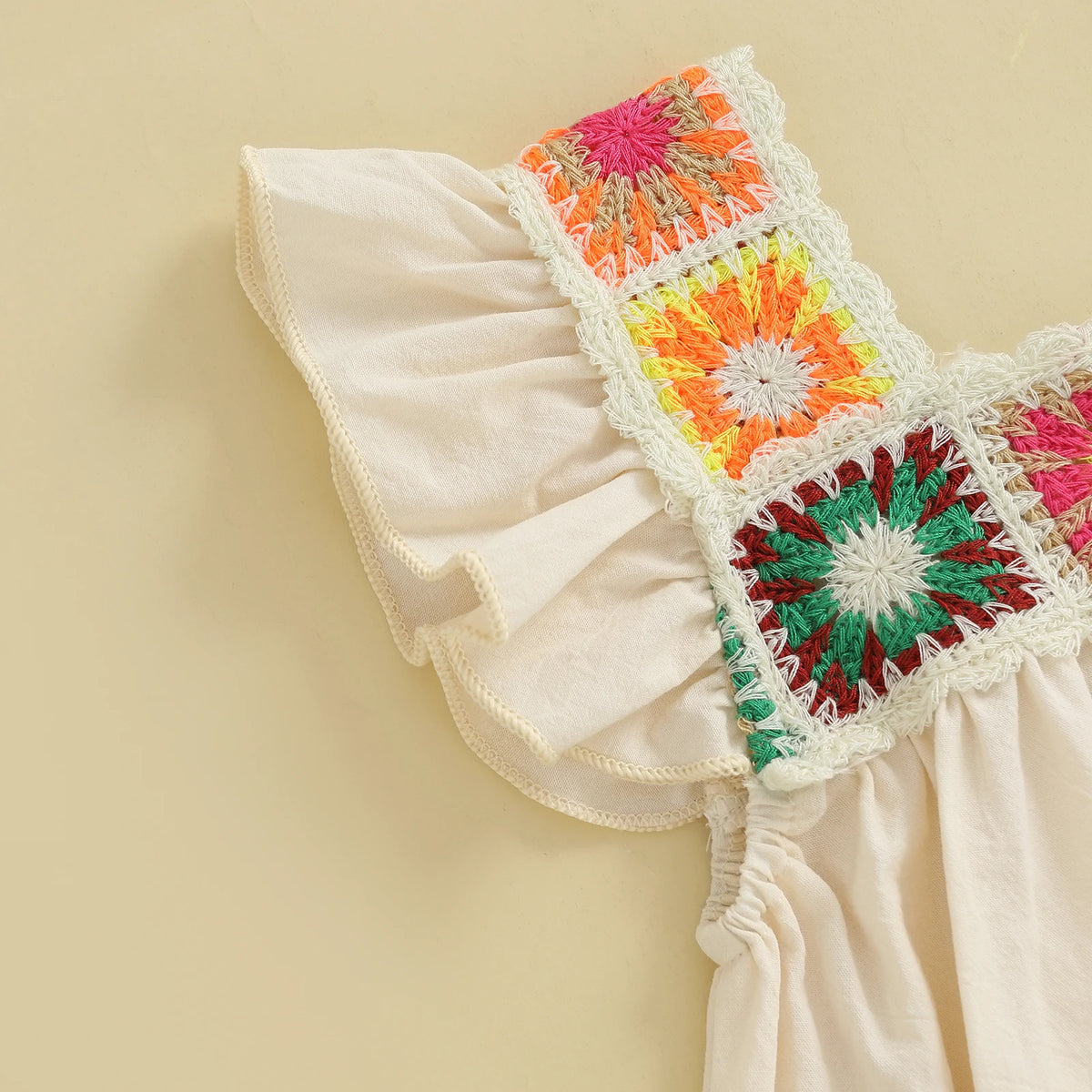 A close-up of a cream colored toddler romper featuring colorful floral embroidery details on the bodice.