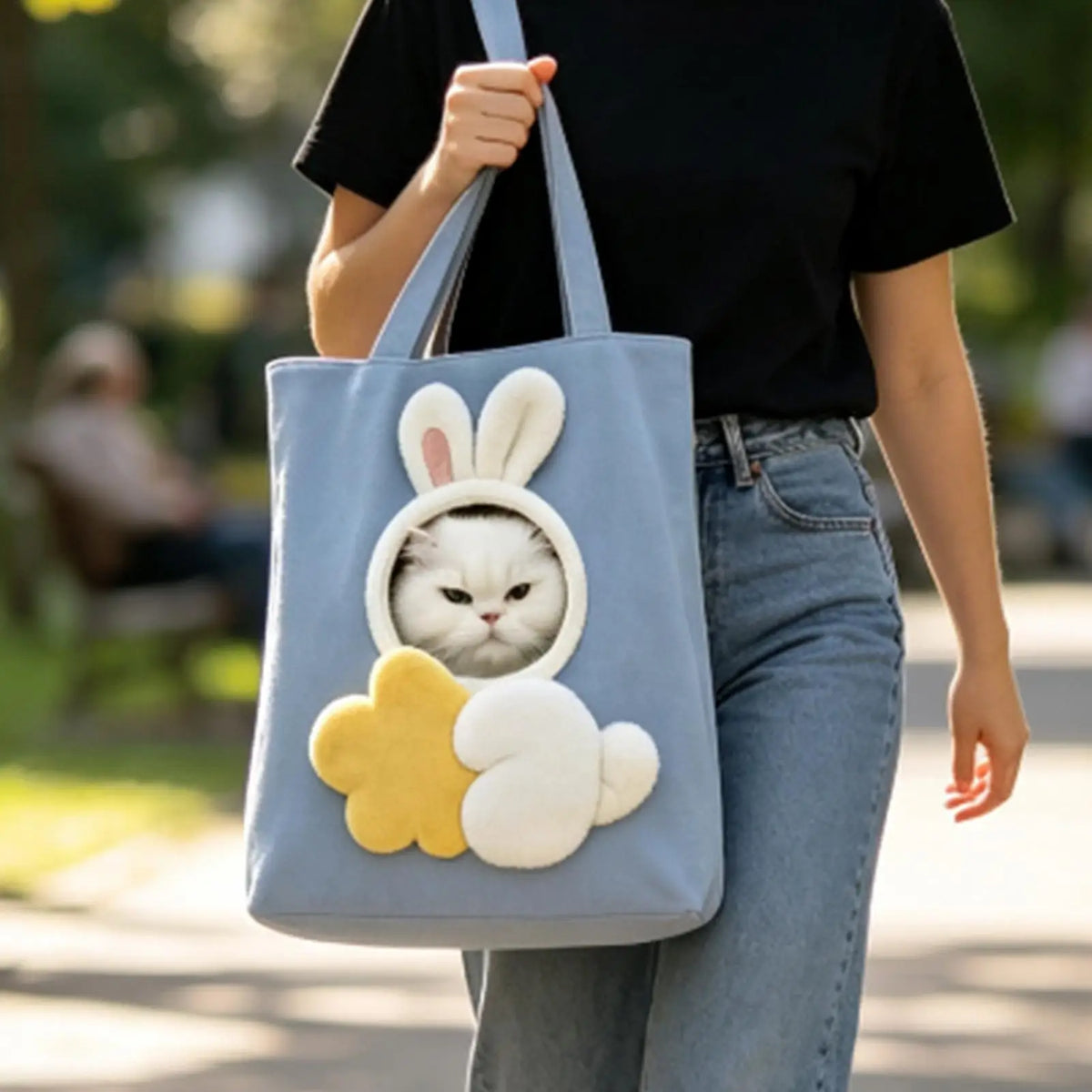 A person is carrying a light blue canvas pet carrier bag featuring cute white rabbit and cloud patterns.