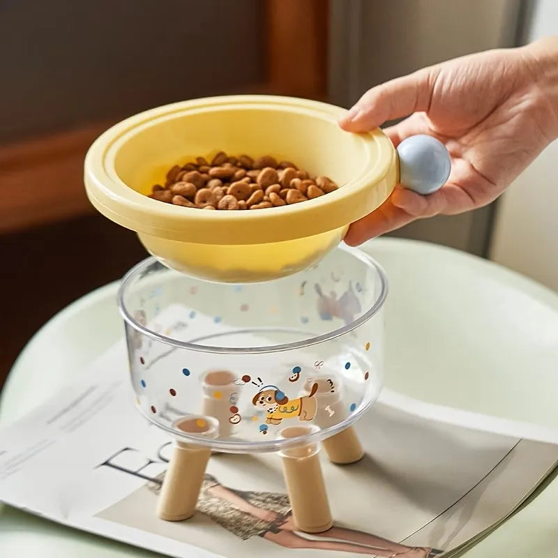 A hand is holding a yellow elevated stainless steel pet bowl with a stand, filled with kibble.