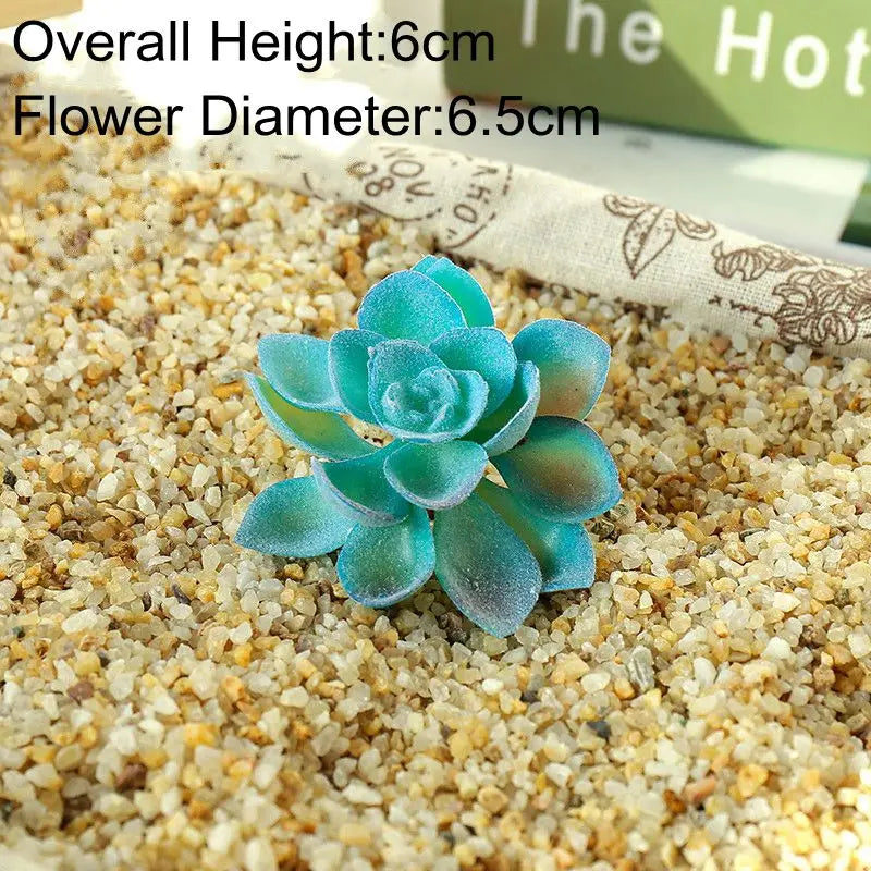 A small, vibrant blue artificial succulent plant resting on a bed of light tan sand.