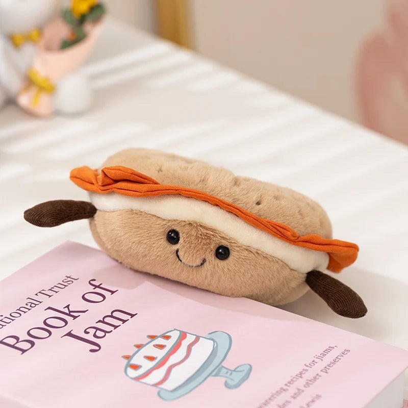 A soft, brown plush toy shaped like a sandwich with an orange slice on top, resting on a pink book.