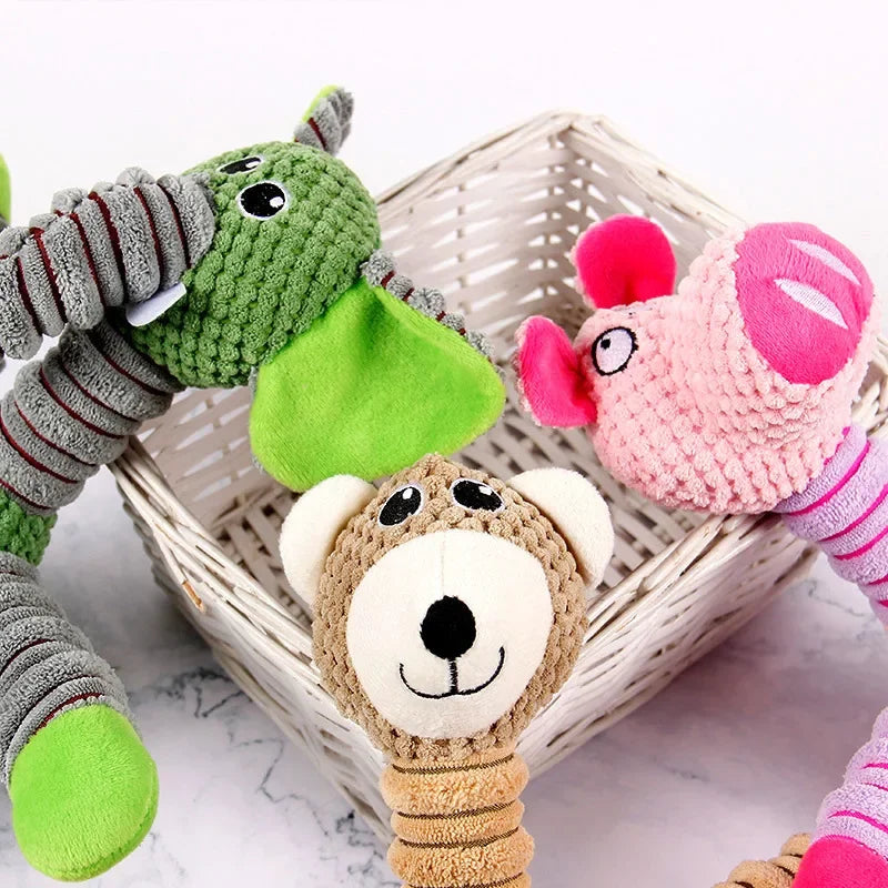 Eine Sammlung weicher Plüsch-Hundesspielzeuge, darunter ein grauer Elefant, ein grüner Elefant und ein rosa-lila Affe, präsen