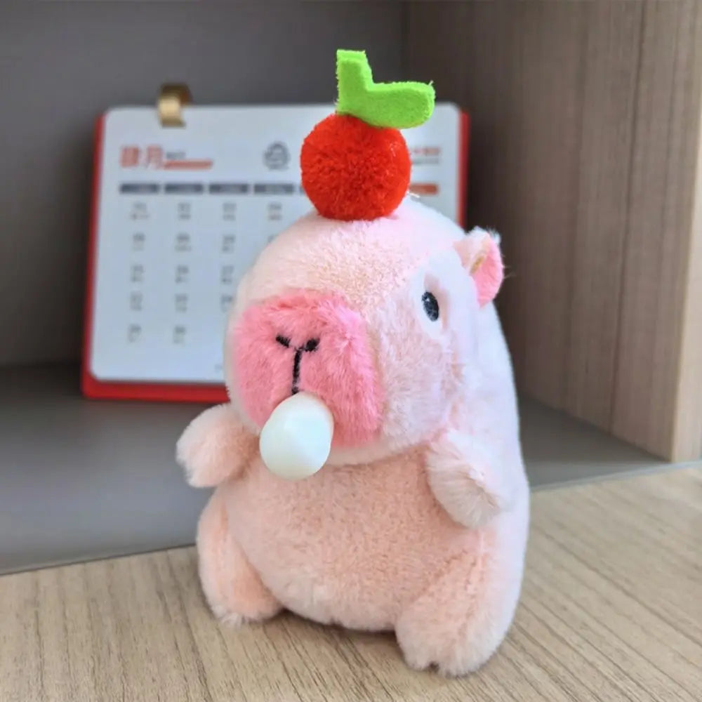 Rosa Capybara-Plüschtier mit grünen Ohren und orangefarbenem Pompon auf Holzoberfläche.