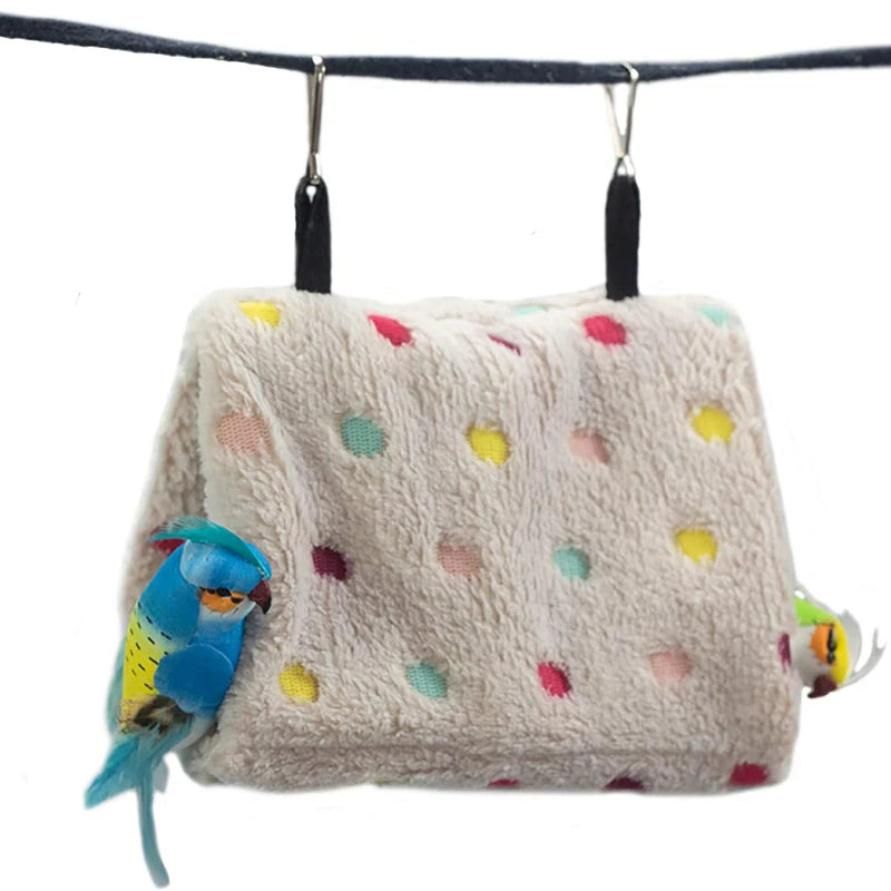 A light beige plush parrot hammock bed with colorful polka dots and a blue parrot figurine hanging from a black cord.