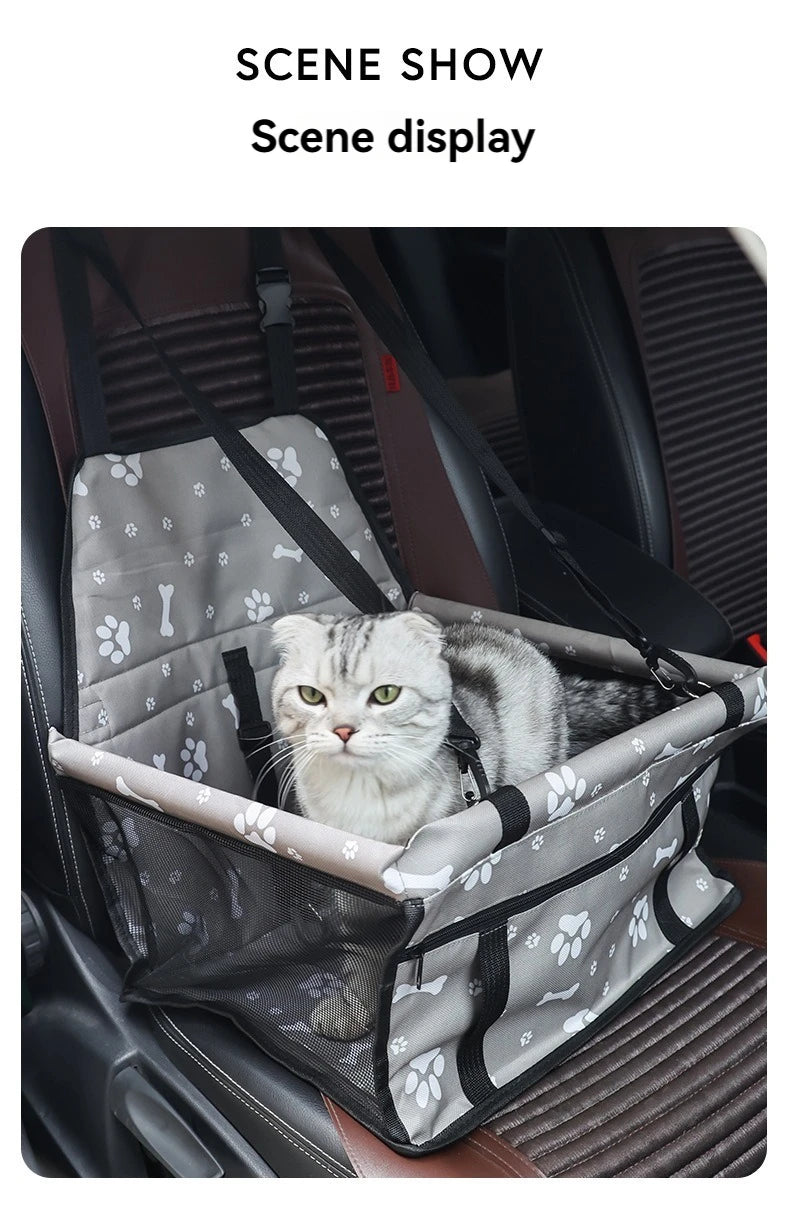 A fluffy gray cat is resting inside a pet travel booster seat with a safety belt, displayed in a car interior.