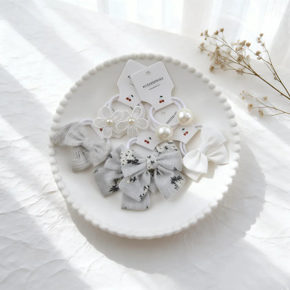 Une assiette blanche présente divers nœuds élastiques pour cheveux gris et blanc, y compris des nœuds en tissu et des accents